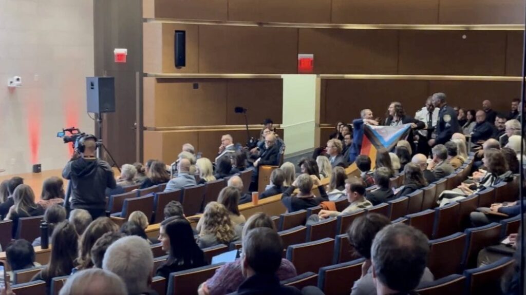 Fight for the Future's Evan Greer holds a pride flag while being forcefully removed from an auditorium.